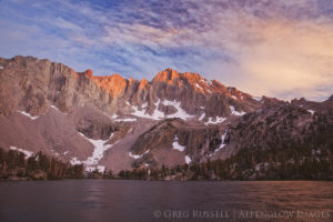 photograph of a mountain peak with the last rays of sunset on it, with colorful clouds above mixed with smoke from a nearby wildfire