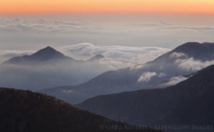the san gabriel mountains rise above fog and clouds in the los angeles basin at sunset