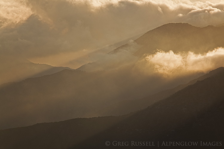 the san gabriel mountains rise above fog and clouds in the los angeles basin at sunset