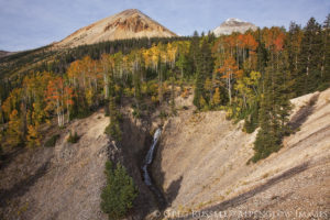 photograph of two mountain peaks in the tushar mountains of utah. Golden and red aspen trees as well as a small waterfall are in the foreground.