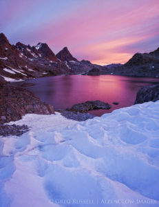 A very colorful sunrise over a high mountain lake in the Sierra Nevada, with snow and sun cups in the foreground