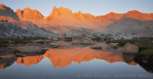 Photograph of high Sierra Nevada peaks being illuminated at sunrise with their reflection in an alpine lake